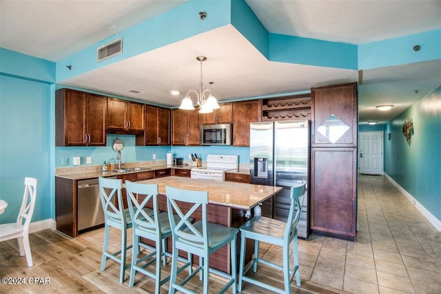 kitchen with a notable chandelier, stainless steel appliances, a kitchen island, and light hardwood / wood-style floors