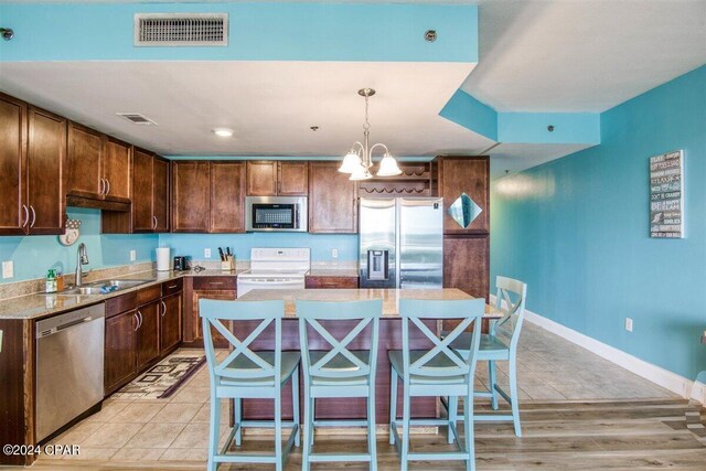 kitchen with a chandelier, appliances with stainless steel finishes, sink, light hardwood / wood-style floors, and a kitchen island