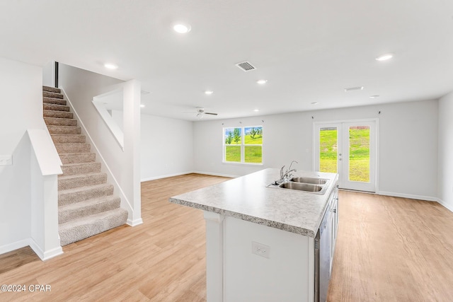 kitchen with french doors, ceiling fan, light hardwood / wood-style floors, sink, and a center island with sink