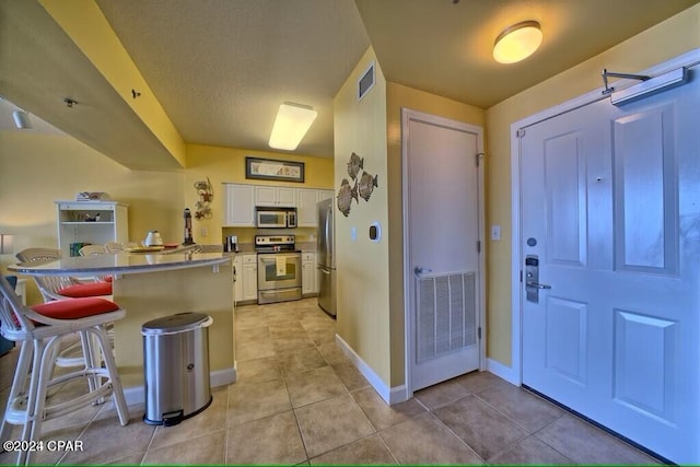 kitchen with light tile patterned flooring, a breakfast bar, stainless steel appliances, and white cabinets