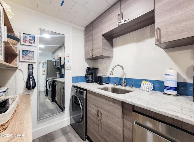 kitchen with hardwood / wood-style floors, sink, appliances with stainless steel finishes, light stone countertops, and washer / dryer