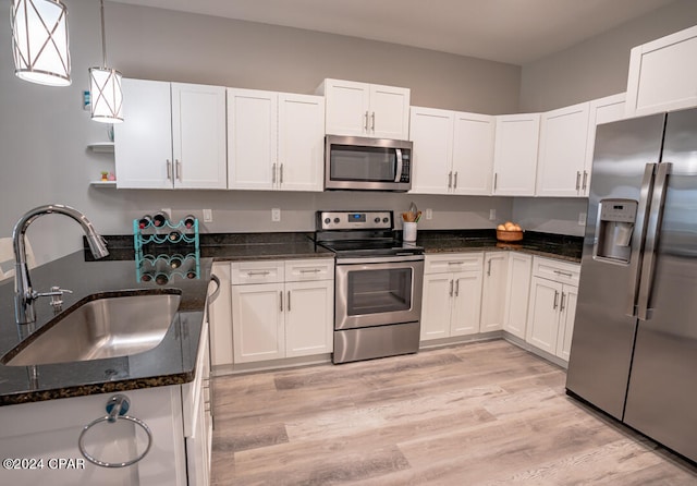 kitchen featuring stainless steel appliances, dark stone countertops, light hardwood / wood-style floors, hanging light fixtures, and sink