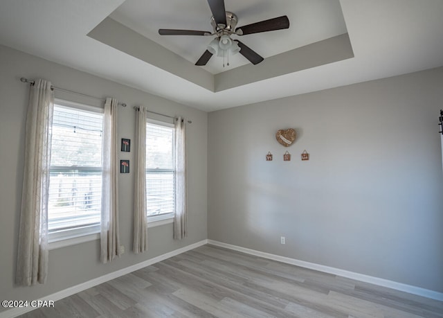 unfurnished room featuring light hardwood / wood-style floors, ceiling fan, and a raised ceiling