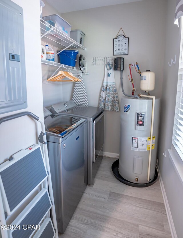 clothes washing area with electric panel, light wood-type flooring, water heater, and washer and clothes dryer