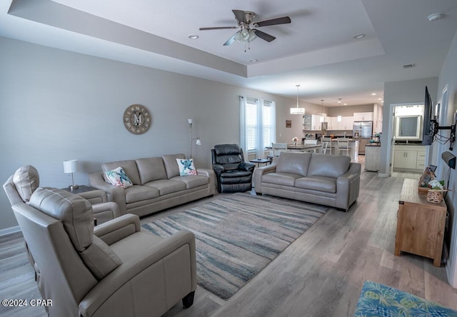 living room featuring ceiling fan, a tray ceiling, and light wood-type flooring