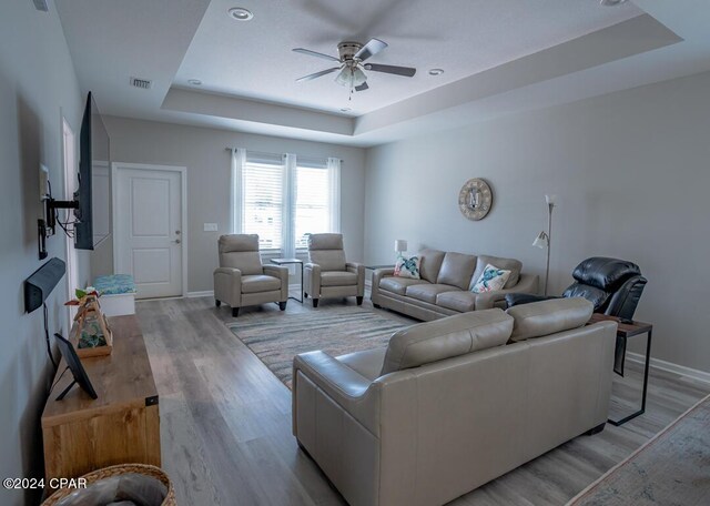 living room with ceiling fan, light wood-type flooring, and a tray ceiling