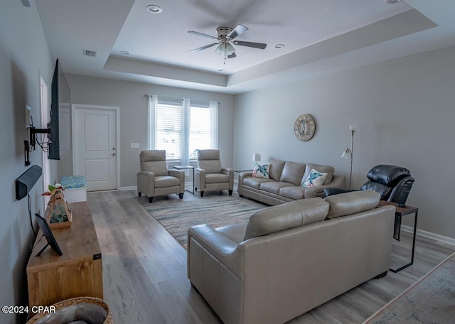 living room featuring a raised ceiling, ceiling fan, and light wood-type flooring