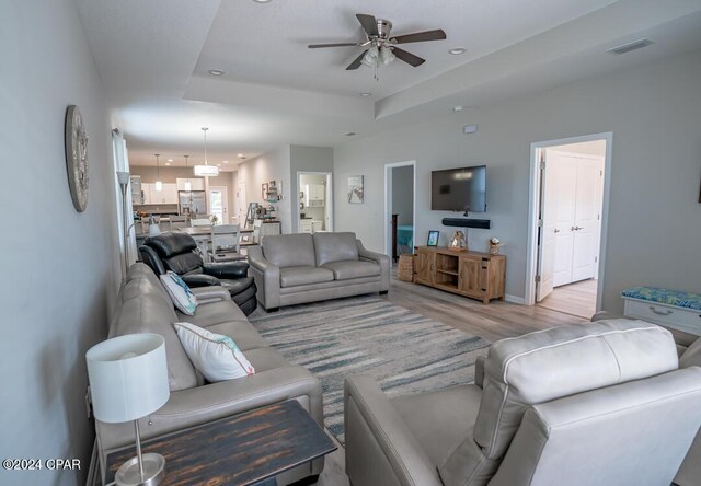 living room with ceiling fan, light hardwood / wood-style flooring, and a raised ceiling