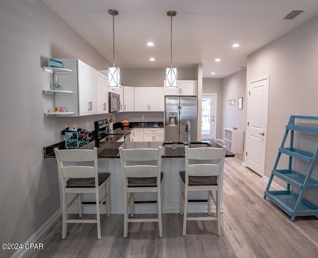 kitchen with appliances with stainless steel finishes, white cabinetry, light hardwood / wood-style flooring, sink, and decorative light fixtures