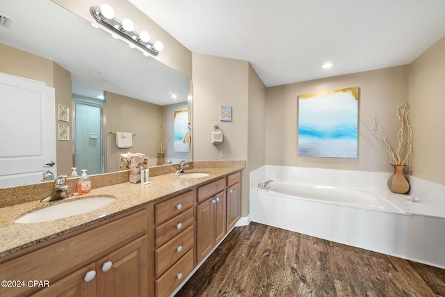 bathroom featuring hardwood / wood-style flooring, dual bowl vanity, and a tub to relax in