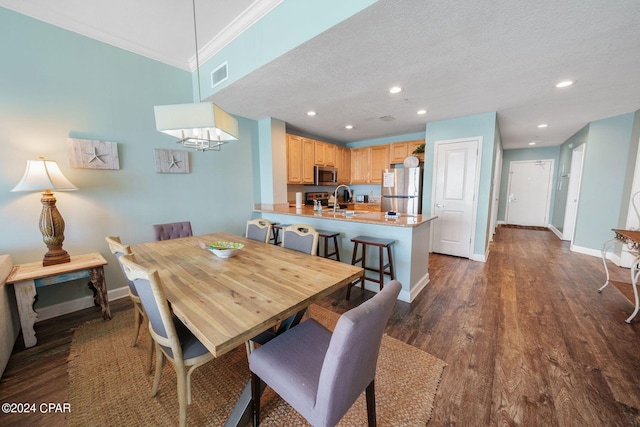 dining space featuring sink, a textured ceiling, crown molding, and dark wood-type flooring