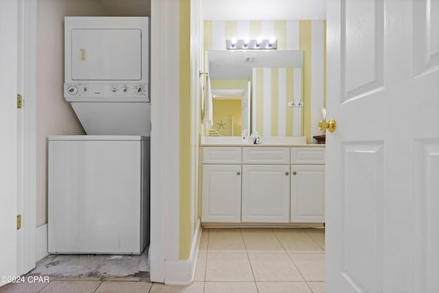 clothes washing area featuring light tile patterned floors, laundry area, stacked washer / dryer, baseboards, and wallpapered walls