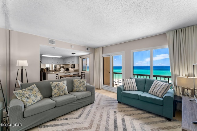 living room with a water view, light hardwood / wood-style floors, and a textured ceiling