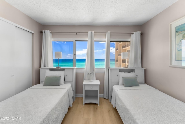 bedroom featuring a water view, a closet, light hardwood / wood-style floors, and a textured ceiling