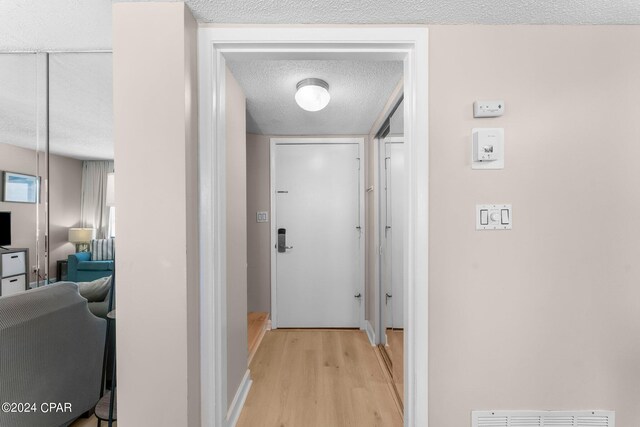 corridor with a textured ceiling and light hardwood / wood-style flooring