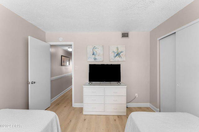 bedroom with light hardwood / wood-style floors, a textured ceiling, and a closet