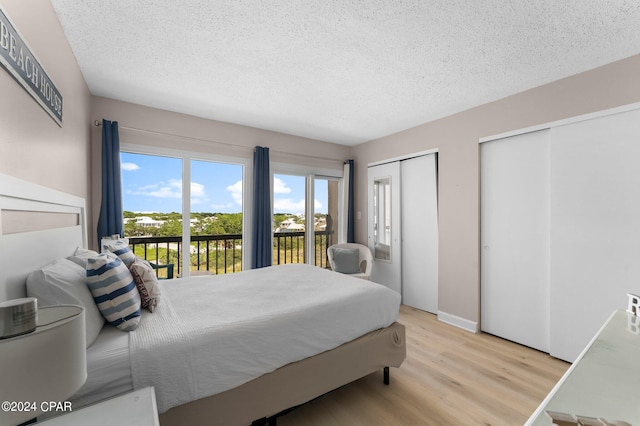 bedroom with a textured ceiling, access to exterior, two closets, and light hardwood / wood-style floors