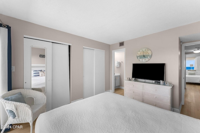 bedroom featuring two closets, wood-type flooring, and ensuite bath