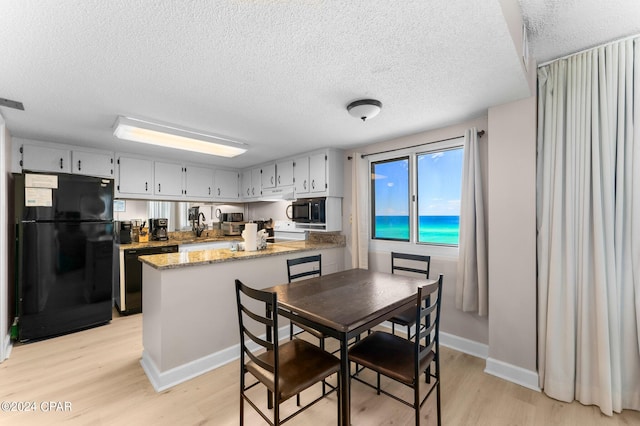 kitchen with a textured ceiling, stone counters, black appliances, and light wood-type flooring