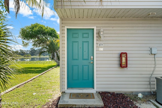 view of exterior entry featuring a water view and a yard