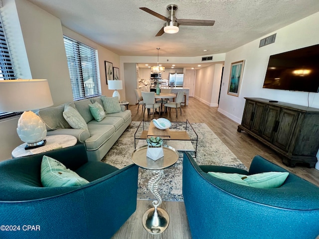 living room with ceiling fan, light wood-type flooring, and a textured ceiling