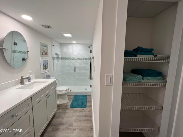 bathroom featuring hardwood / wood-style flooring, a shower with shower door, vanity, and toilet