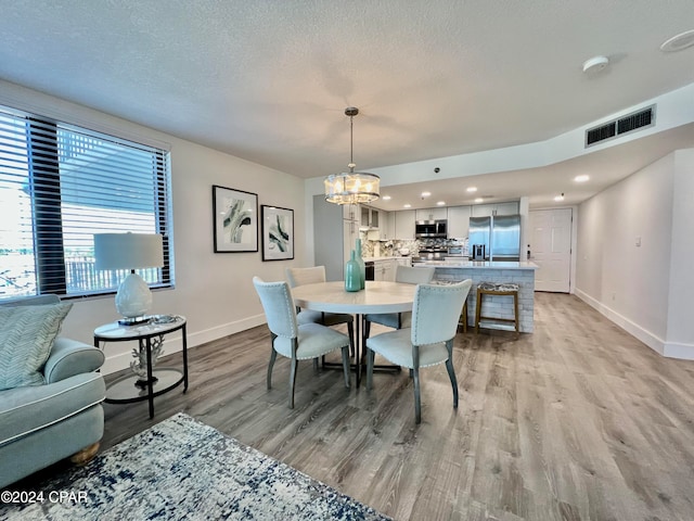 dining space with a textured ceiling, a notable chandelier, and light hardwood / wood-style floors