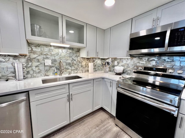 kitchen with appliances with stainless steel finishes, backsplash, sink, light wood-type flooring, and light stone countertops