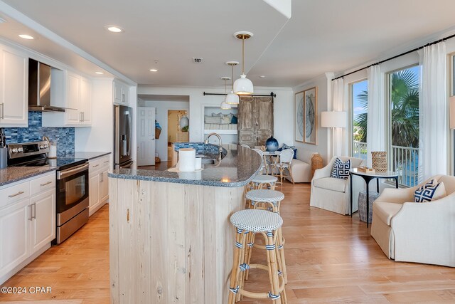 kitchen featuring backsplash, stainless steel appliances, light hardwood / wood-style flooring, wall chimney range hood, and a breakfast bar area