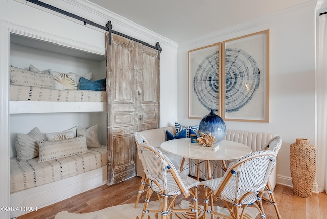 dining area with a barn door, wood-type flooring, and crown molding