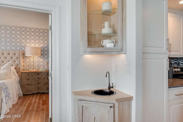 bar featuring sink, light hardwood / wood-style floors, white cabinetry, and dark stone counters