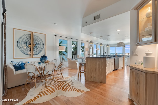 kitchen with a breakfast bar area, decorative light fixtures, stainless steel dishwasher, and light wood-type flooring