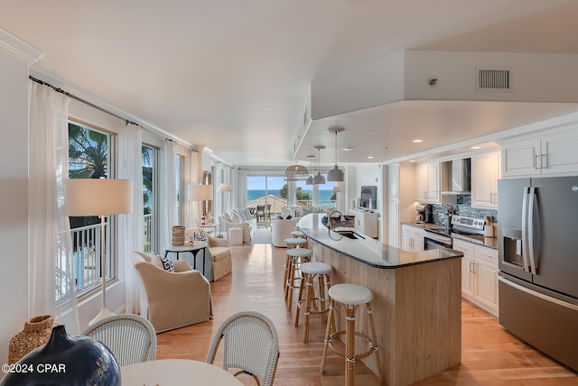 kitchen featuring a breakfast bar area, stainless steel appliances, white cabinets, and light hardwood / wood-style flooring