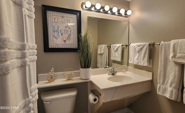 bathroom with a textured wall, vanity, and toilet