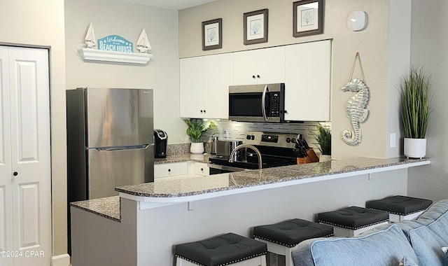 kitchen with a peninsula, appliances with stainless steel finishes, a breakfast bar, and white cabinets