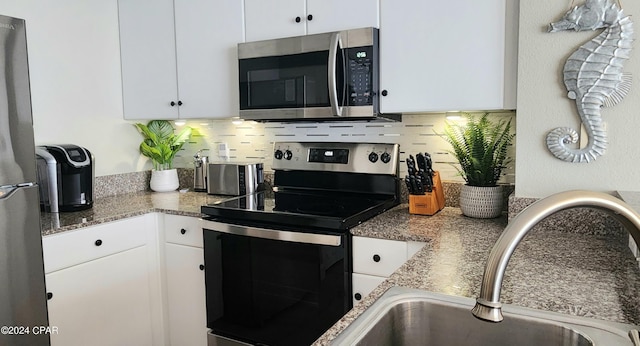 kitchen with stone countertops, stainless steel appliances, a sink, white cabinets, and backsplash