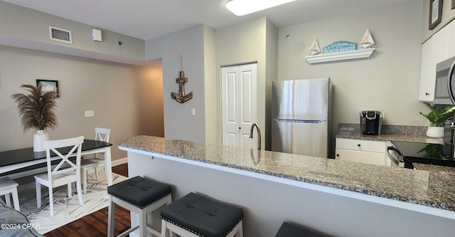 kitchen with visible vents, white cabinets, appliances with stainless steel finishes, a breakfast bar, and a peninsula