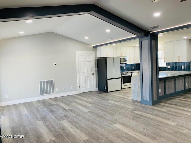 kitchen featuring white cabinetry, stainless steel stove, lofted ceiling with beams, and white fridge