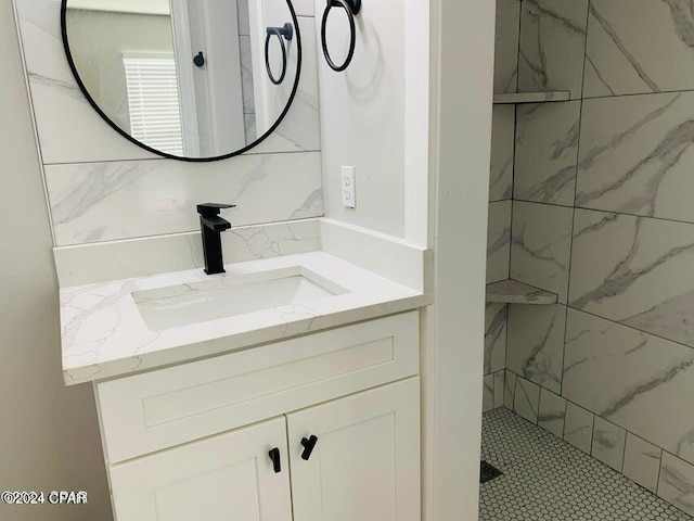 bathroom with a tile shower, vanity, and decorative backsplash