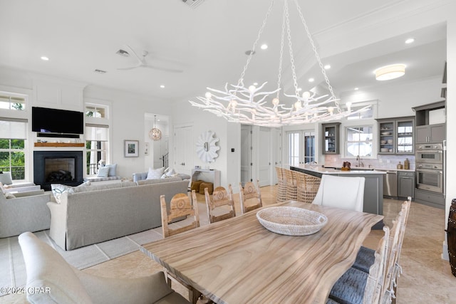 tiled dining space featuring crown molding, sink, and ceiling fan with notable chandelier