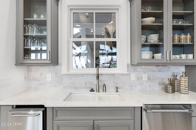 kitchen with stainless steel dishwasher, gray cabinets, light stone countertops, and sink