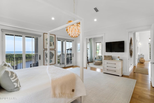 bedroom with access to exterior, a water view, multiple windows, and light hardwood / wood-style floors