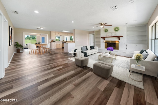 living room featuring a textured ceiling, a brick fireplace, ceiling fan, and dark wood-type flooring