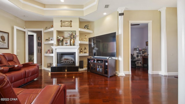 living room with built in shelves, dark hardwood / wood-style floors, crown molding, decorative columns, and a tray ceiling