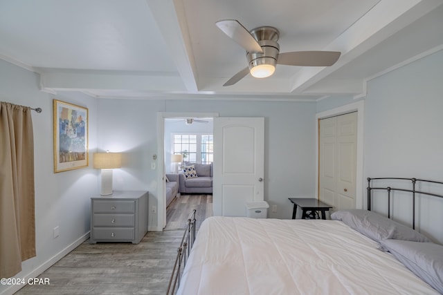 unfurnished bedroom with a closet, ceiling fan, beamed ceiling, and light wood-type flooring