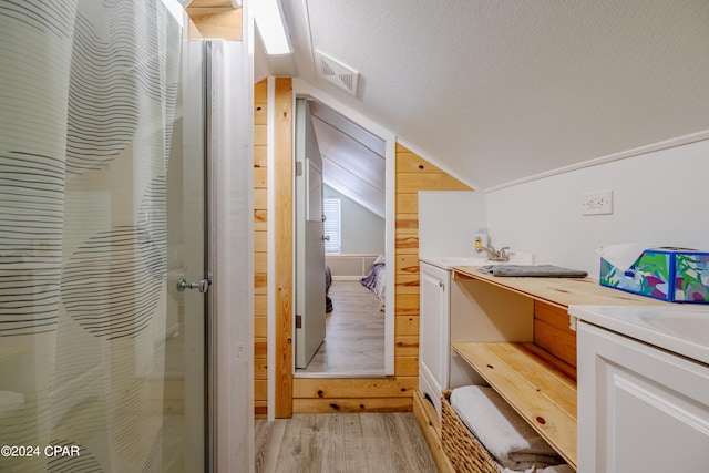 bathroom with a textured ceiling, hardwood / wood-style floors, lofted ceiling, vanity, and wooden walls