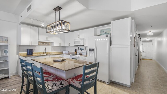 kitchen with white appliances, a breakfast bar, light stone counters, sink, and a kitchen island