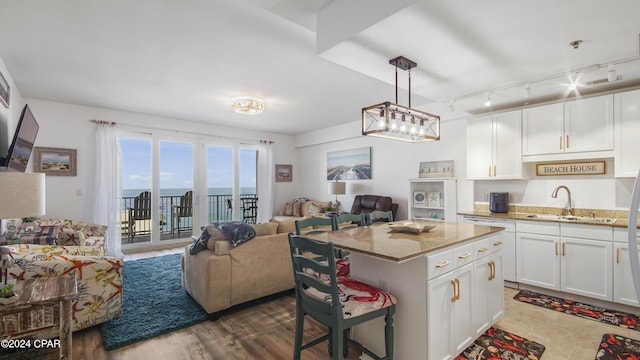 kitchen featuring a kitchen island, a breakfast bar, pendant lighting, sink, and white cabinets