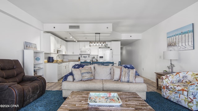 living room featuring rail lighting, sink, an inviting chandelier, and light hardwood / wood-style flooring