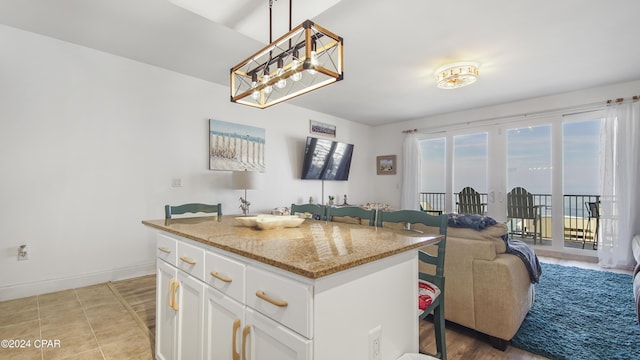 kitchen featuring light stone counters, a center island, hanging light fixtures, light tile patterned floors, and white cabinets